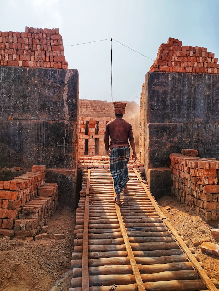 A worker carries bricks in a rustic brick factory setting. Industrial and cultural themes.